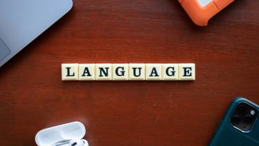 Scrabble tiles spelling out the word "language" on a brown desk.